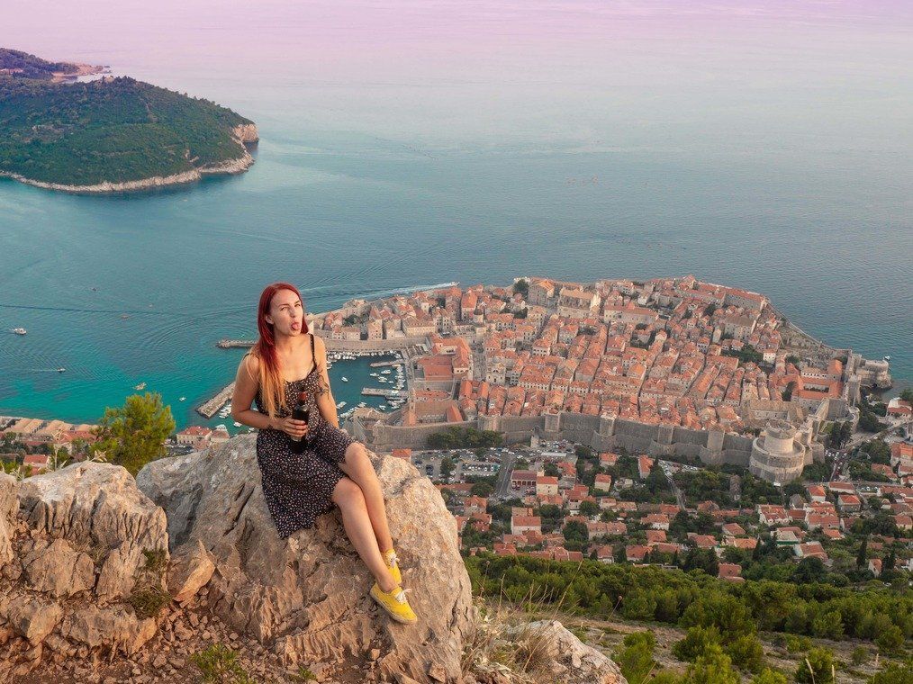 mochilera sola mirando a Dubrovnik, Croacia, con una botella de vino en la mano